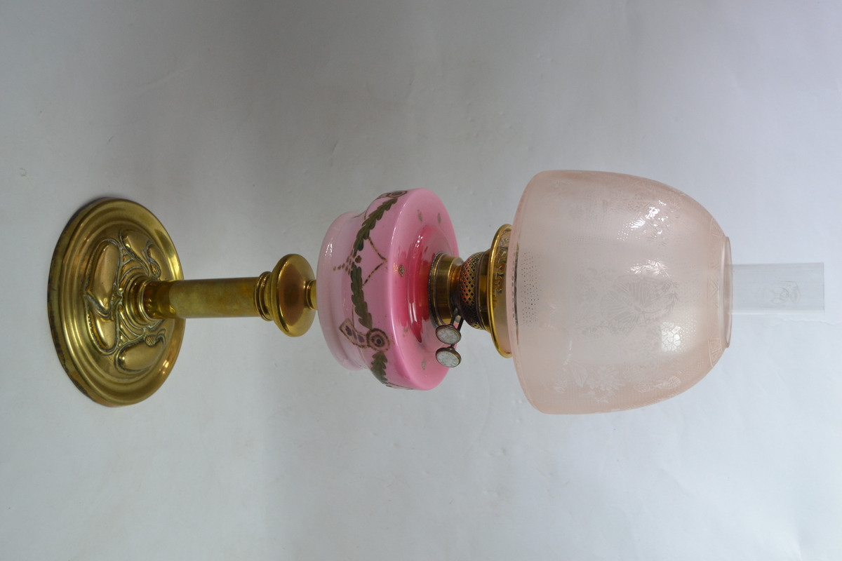 An Art Nouveau Brass Based Oil Lamp With Enamel Painted Cranberry Ceramic reservoir
